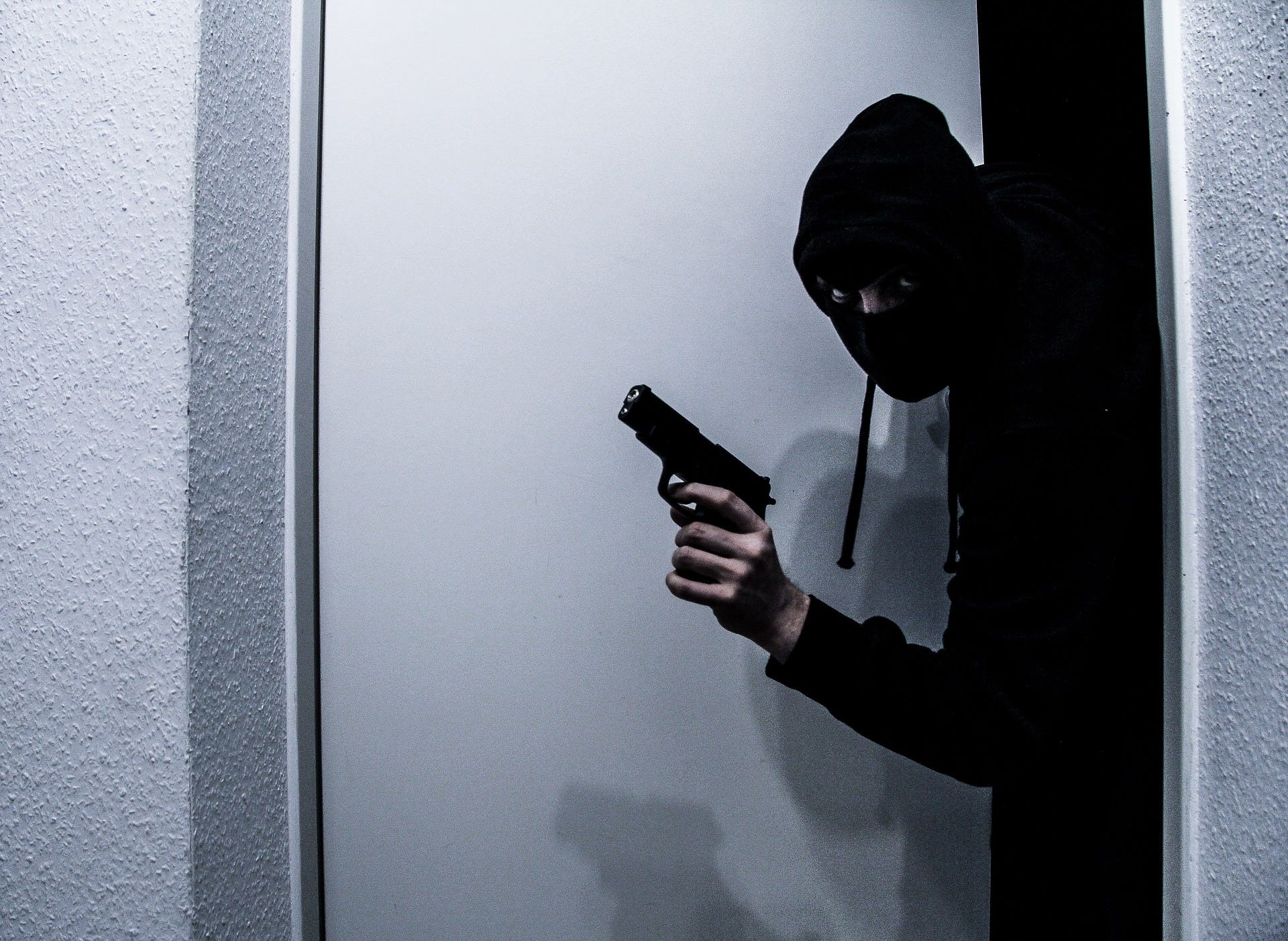 A burgler with a gun exits a doorway.