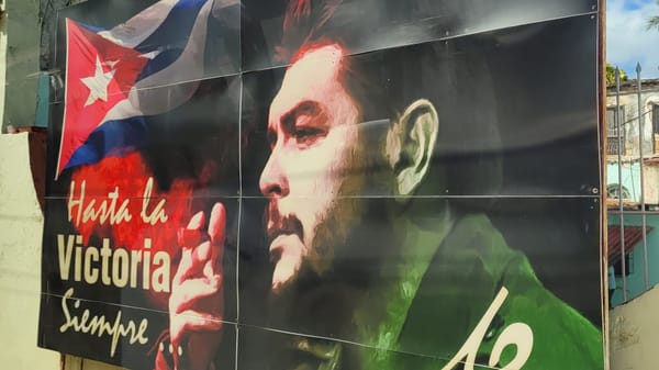 A billboard in Cuba shows a picture of Che Guevara, as the Cuban flag waves. Words read "Hasta la Victoria Siempre..." (Always forward to victory)