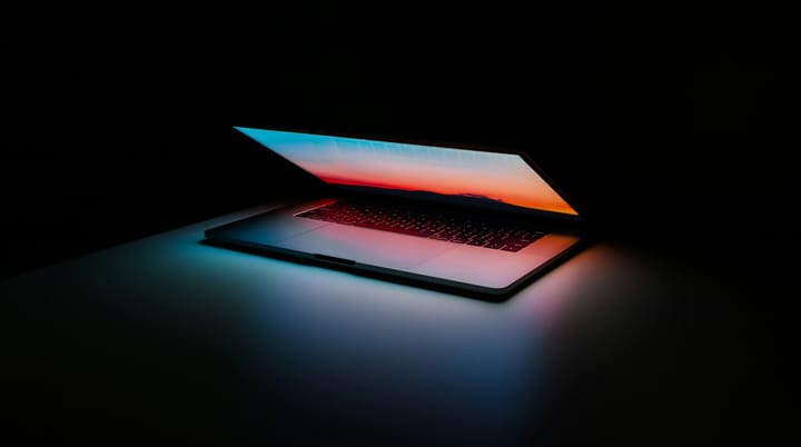 A laptop sitting in a dark room, half-open and shining its light on the keyboard.