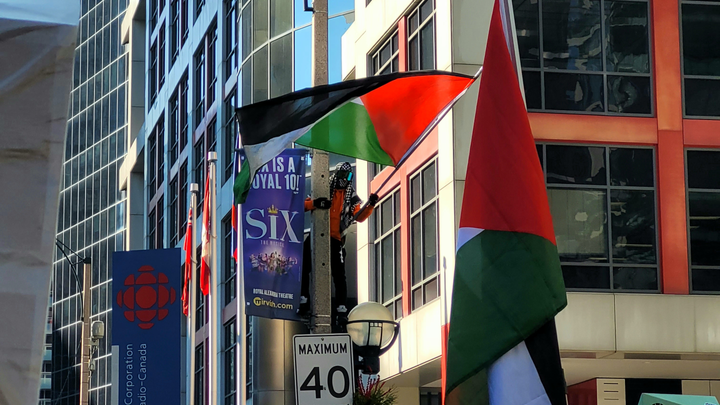 A protestor waves a Palestinian flag on a streetlight post in front of the CBC News HQ in downtown Toronto