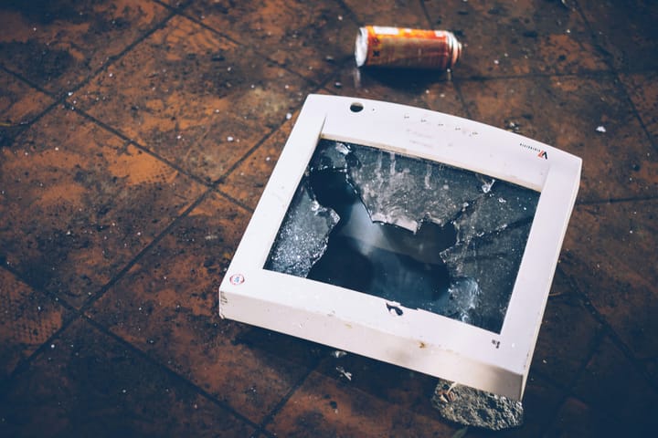A smashed computer monitor lays on a brown tiled floor. An empty can rests on the floor beside it.