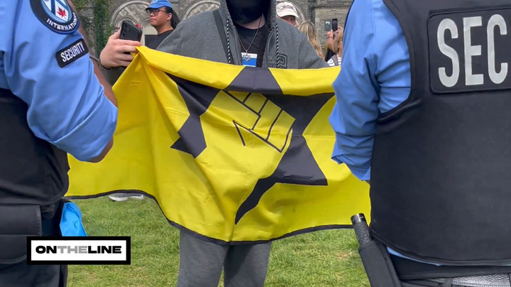 A pro-Israel protestor in a hoodie and a mask waves a Kahanist flag, while two UofT security personnel are on each side