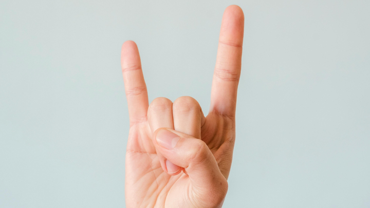 A hand doing the devil horns gesture on a grey background