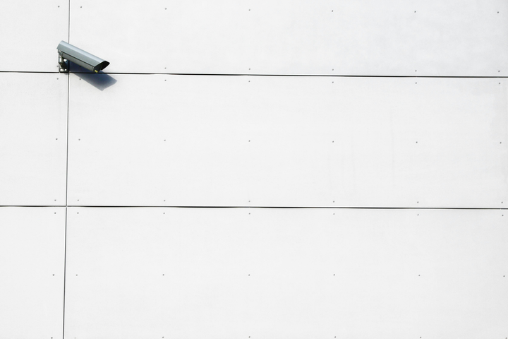 A surveillance camera on a wall looks to the side